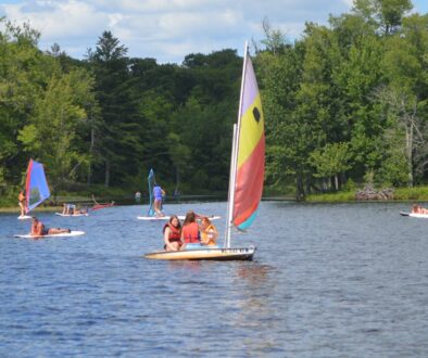Campers at WeHaKee Camp for Girls having fun boating, sailing, and paddle boarding on Hunter Lake