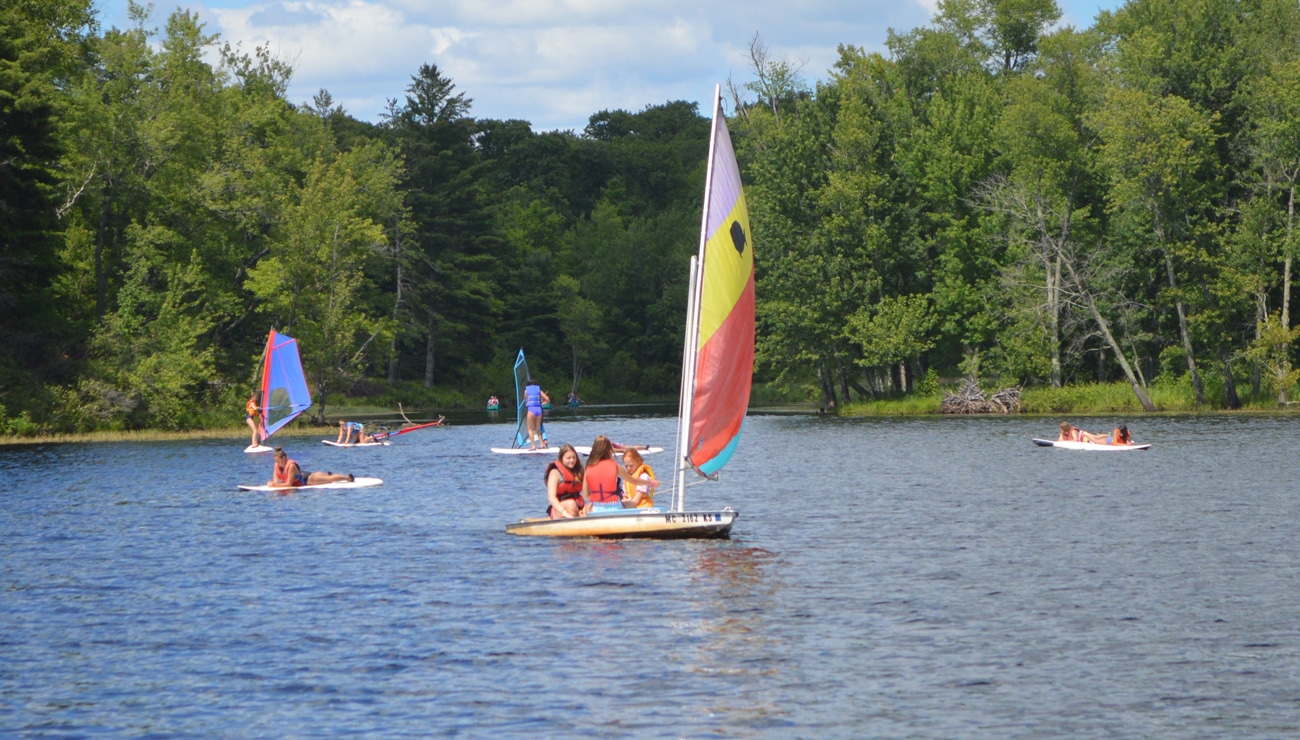 Campers at WeHaKee Camp for Girls having fun boating, sailing, and paddle boarding on Hunter Lake