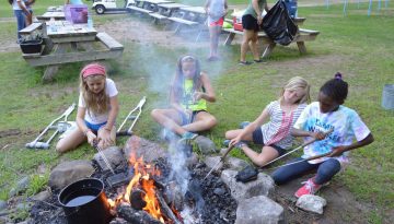 Campers making pudgy pies at the fire for supper at WeHaKee Camp for Girls.