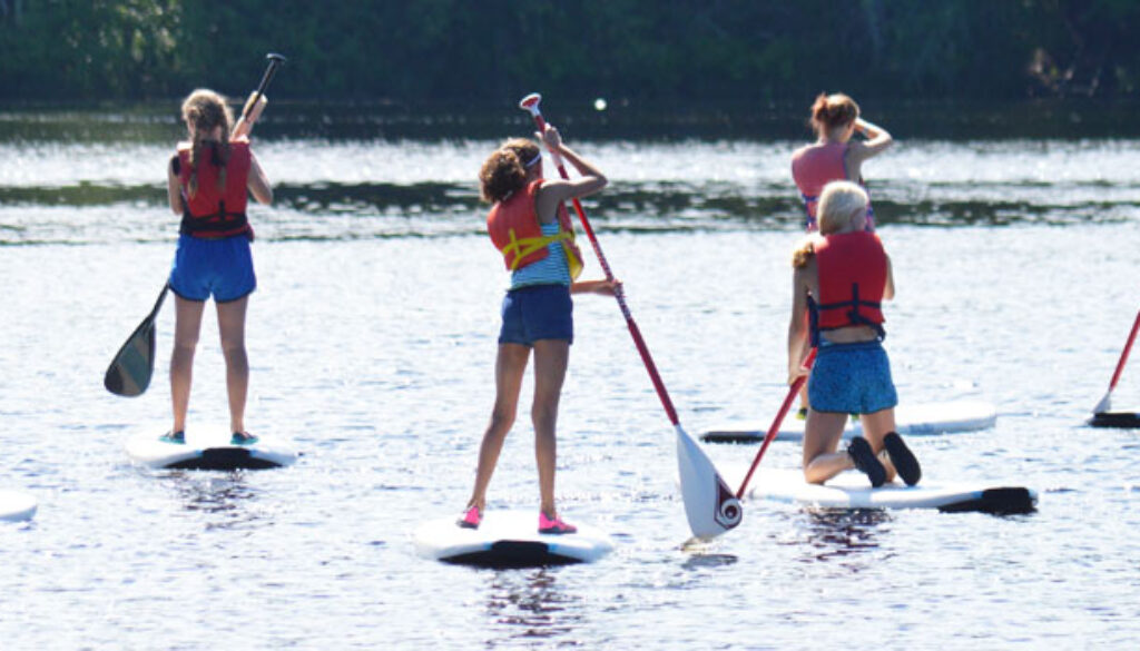 Campers at WeHaKee Camp for Girls standing on Paddle board on Hunter Lake.