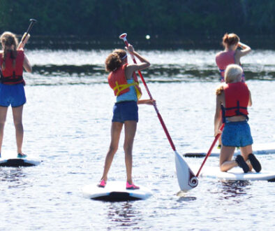 Campers at WeHaKee Camp for Girls standing on Paddle board on Hunter Lake.