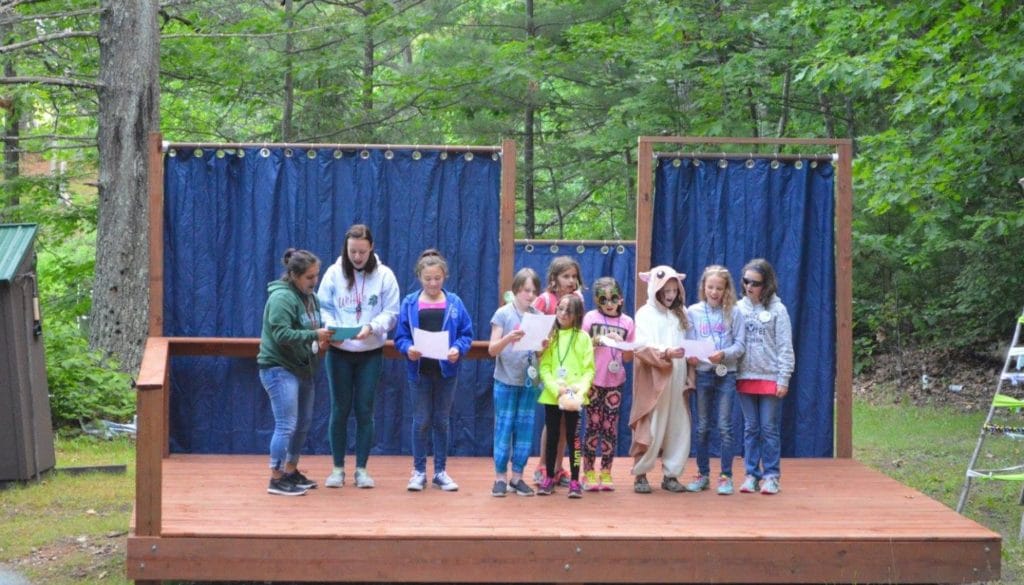 WeHaKee Camp for Girls campers and staff reading a skit on the outdoor stage.