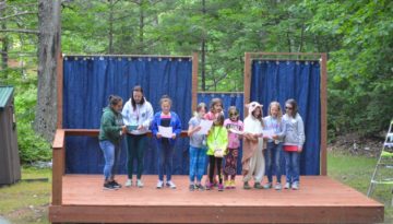 WeHaKee Camp for Girls campers and staff reading a skit on the outdoor stage.