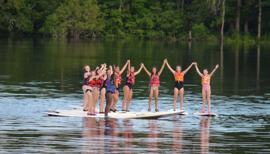 WeHakee Camp for Girls campers holding hands while standing on paddle boards.